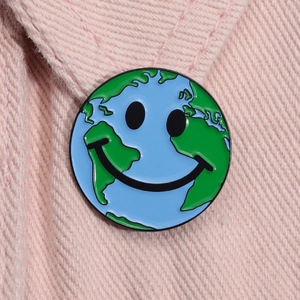 Détail macro du pin's émaillé visage souriant Terre sur un tissu en jean rose clair