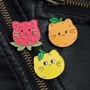 Détail de pins de chat en émail avec motifs fraise, orange et citron sur veste en cuir noir
