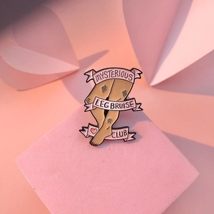 Dettaglio della spilla smaltata Mysterious Leg Bruise Club con nastro rosa su base