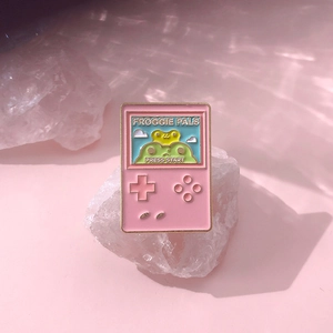 Detail of pink retro game console enamel pin featuring cute green frog characters