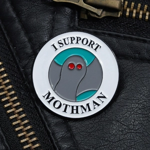 Close-up of a Mothman enamel pin with red eyes on a black leather jacket texture