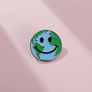 Détail d'un pin's émaillé en forme de Terre avec visage souriant sur fond rose poudré