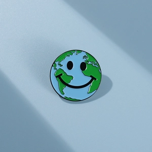 Gros plan détaillé d'un pin's globe terrestre émaillé bleu et vert avec un visage souriant