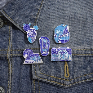 Detail shot of five outdoor adventure enamel pins on a blue denim jacket pocket
