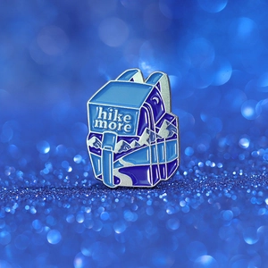 Macro shot of a blue enamel backpack pin featuring a hike more text and mountain scenery