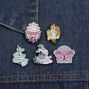 Set of five witch-themed enamel pins including moth and skull on blue denim fabric