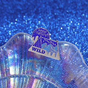 Macro detail of camping enamel pin featuring mountain landscape and keep nature WILD text