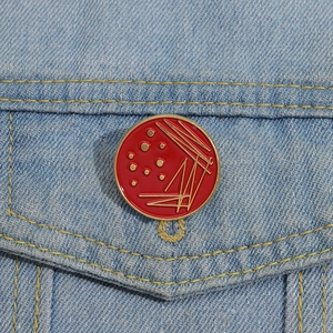 Detail of red enamel petri dish brooch with gold lines on a denim jacket pocket
