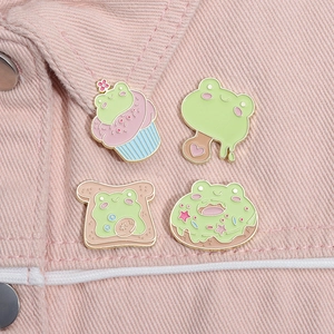 Detalle de cuatro pines de esmalte de ranas y postres sobre una chaqueta rosa
