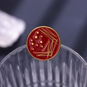 Macro shot of red round petri dish enamel pin with gold bacterial culture patterns