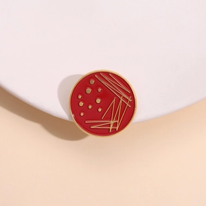 Minimalist red enamel science brooch with golden metal lines showing microbial colony patterns