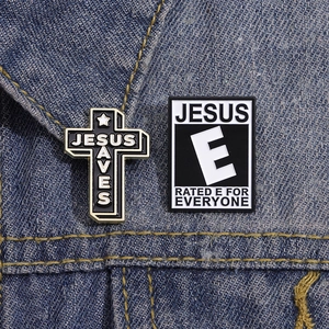 Detail of Jesus Saves cross and Rated E for Everyone enamel pins on blue denim fabric
