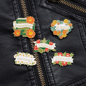 Detailed close-up of five colorful enamel flower and book pins on a black leather jacket