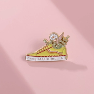 Close-up of enamel sneaker brooch with flowers and Every Step Is Growth quote