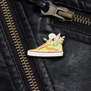 Detail of yellow sneaker enamel pin with flowers and every step is growth quote