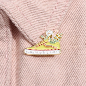 Macro shot of yellow canvas shoe brooch with flowers and Every Step is Growth text