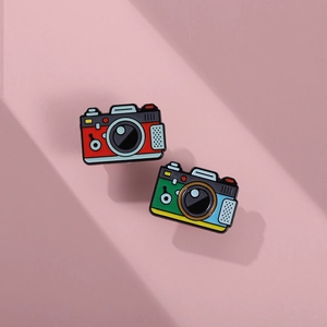 Macro detail of retro camera enamel pins in vibrant colors on a pink background