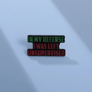 Detail of enamel pin featuring humorous IN MY DEFENSE I WAS LEFT UNSUPERVISED text