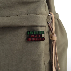 Macro view of a funny quote enamel pin reading IN MY DEFENSE I WAS LEFT UNSUPERVISED