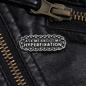 Detailed macro of vintage metal enamel pin with text decoration on black leather jacket