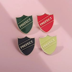 Close-up of four colorful shield enamel pins with gold trim and Prefect lettering