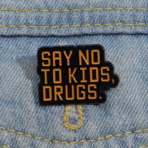 Black enamel pin with orange Say No To Kids Drugs lettering on denim jacket background