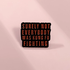 Detail of a black enamel pin with orange text Surely Not Everybody Was Kung Fu Fighting