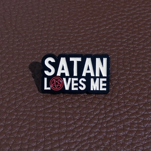 Detail of Satan Loves Me enamel pin with red pentagram star on brown leather background