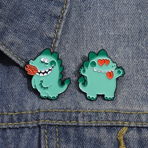 Détail de deux broches en émail petit monstre vert sur une veste en jean bleu foncé