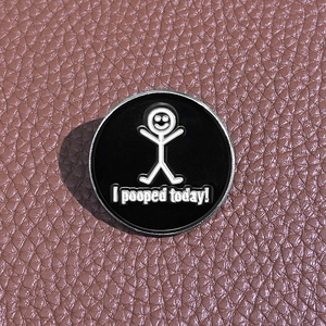 Detailed macro view of a round black enamel pin with white I pooped today text