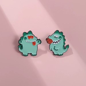 Détail de deux jolies épingles dinosaures en émail vert menthe sur fond rose doux