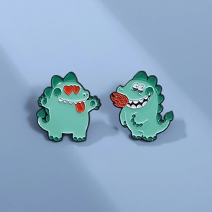 Détail de deux pins émaillés petit monstre vert avec un cœur rouge et un souffle de feu