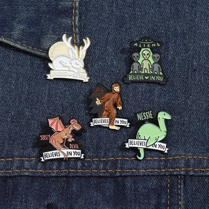 Set of 5 mythical creature enamel pins on blue denim fabric featuring aliens and Bigfoot