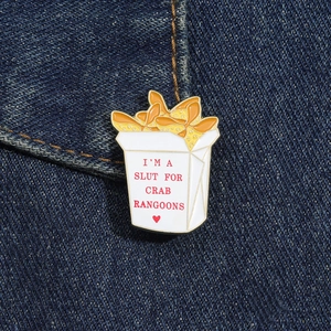 Dettaglio macro della spilla smaltata crab rangoon con testo su tessuto denim scuro