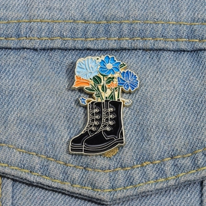 Creative enamel brooch featuring a black boot with blue flowers on denim jacket