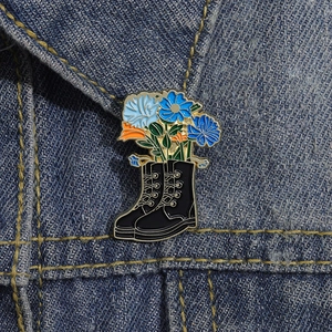 Detail of a floral black leather boot enamel pin on a denim jacket collar