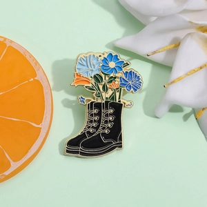 Detail showing a black boot enamel pin with blue flowers on a light mint background