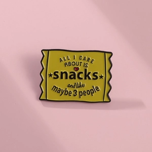 Detailed close-up of a yellow enamel snack pack brooch with witty text on a pink background
