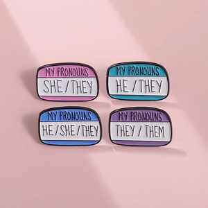 Set of four colorful enamel pronoun pins including She/They on a pink background