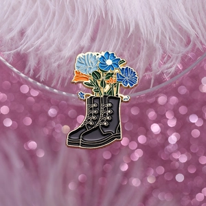 Detail of creative black leather boot brooch with blue flowers on a pink bokeh background