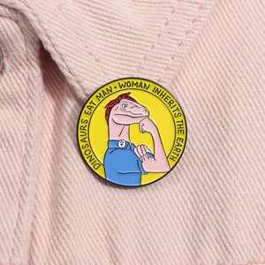 Détail du pin's dinosaure en émail avec slogan féministe sur un fond en jean rose pastel