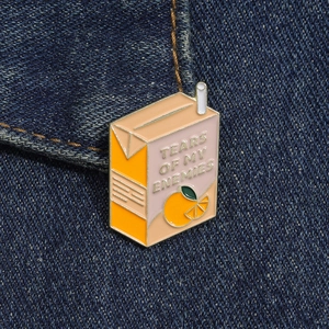 Détail d'un pin's en émail en forme de brique de jus d'orange sur un tissu en denim
