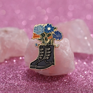 Detailed view of a metal boot brooch with blue flowers resting on pink crystals