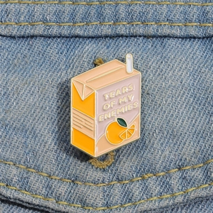 Détail du pin's en émail boîte de jus d'orange avec texte sur du tissu en denim bleu