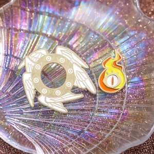 Macro detail of enamel pins featuring a golden seraphim angel and flaming eyeball