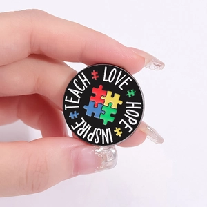 Rainbow puzzle heart enamel pin with Teach Love Hope Inspire text on black base