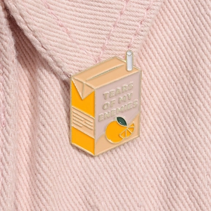 Détail d'un pin's en émail boîte de jus d'orange sur une veste en jean rose avec slogan