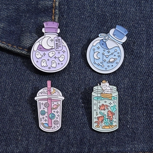 Detail of four creative enamel pins with ghost bottles and space tea designs on denim fabric