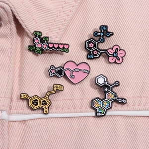 Détail de cinq pin's émaillés aux molécules chimiques et motifs de cœur sur tissu rose