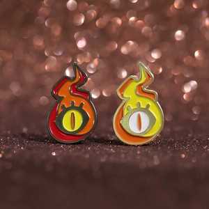 Enamel pins featuring flame-shaped eyes in red and yellow with bokeh background